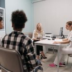Médicos conversam com pacientes durante uma consulta em uma sala de clínica.
