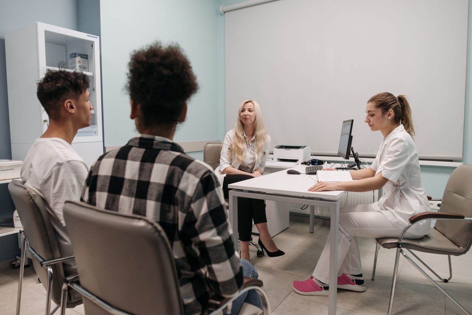 Médicos conversam com pacientes durante uma consulta em uma sala de clínica.
