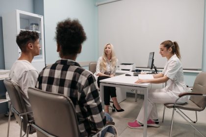 Médicos conversam com pacientes durante uma consulta em uma sala de clínica.