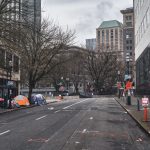 Barracas instaladas em uma rua urbana, sob árvores sem folhas, evidenciam uma área de ocupação por pessoas em situação de rua.