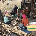 Grupo de pessoas confecciona produtos de bambu ao ar livre, em uma atividade comunitária de produção artesanal.