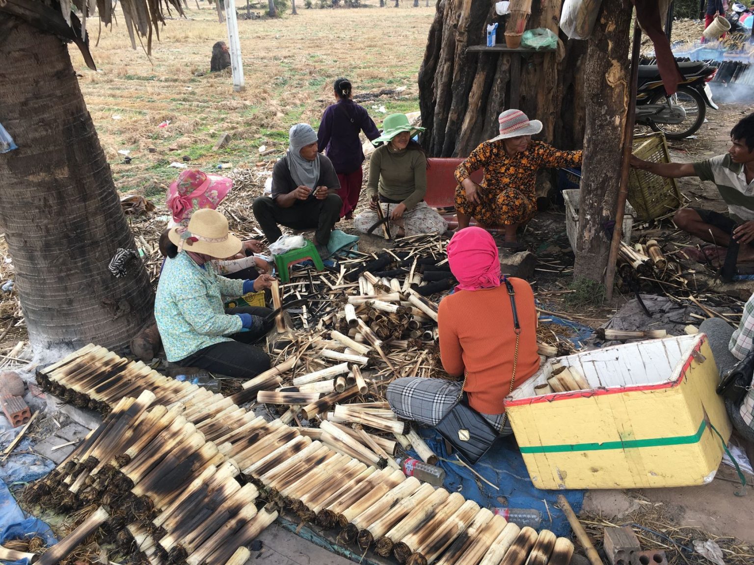 Grupo de pessoas confecciona produtos de bambu ao ar livre, em uma atividade comunitária de produção artesanal.
