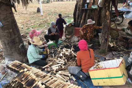 Grupo de pessoas confecciona produtos de bambu ao ar livre, em uma atividade comunitária de produção artesanal.