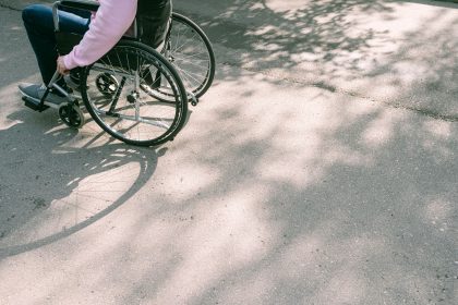 Pessoa em cadeira de rodas se desloca por uma via urbana arborizada, sob a sombra das árvores.