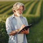 Homem em um campo verde registra informações em uma prancheta durante uma fiscalização rural.