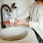 Mulher enche um copo com água em uma torneira de cozinha.