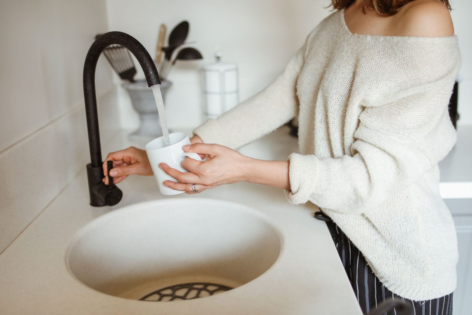 Mulher enche um copo com água em uma torneira de cozinha.