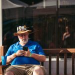 Homem idoso usando um smartphone sentado em um banco ao ar livre.