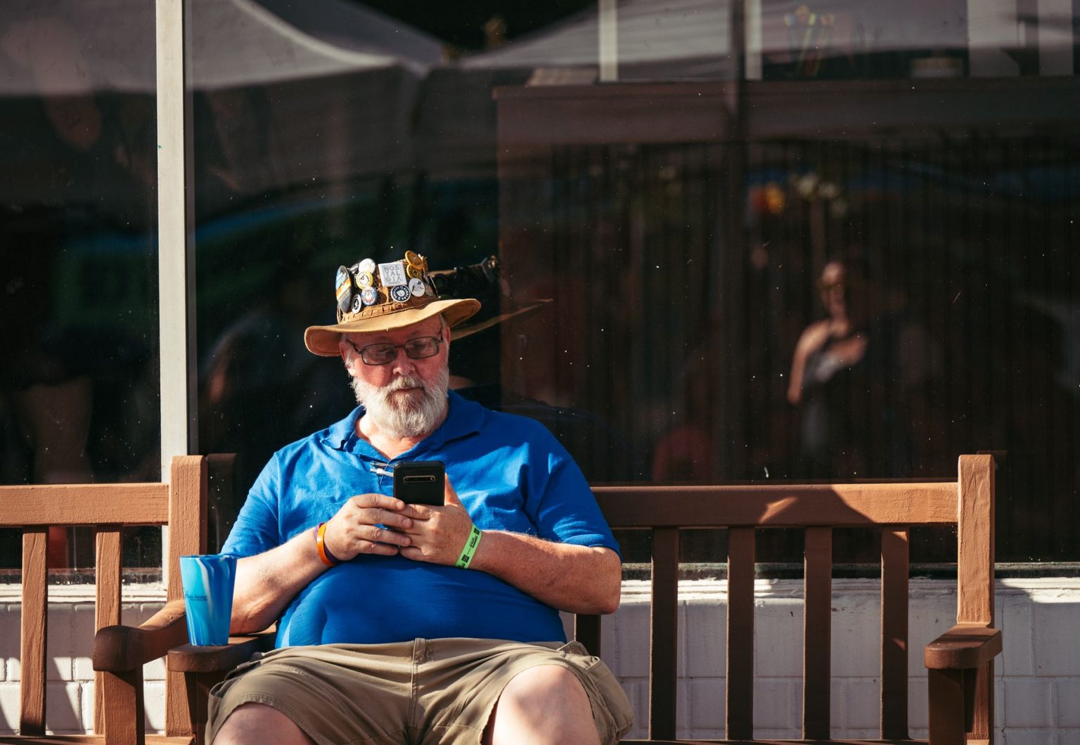 Homem idoso usando um smartphone sentado em um banco ao ar livre.