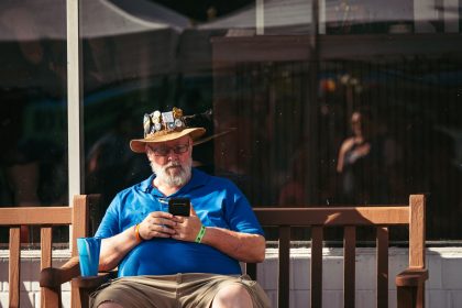 Homem idoso usando um smartphone sentado em um banco ao ar livre.