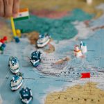 Mapa-múndi com pequenos navios e bandeiras indicando diferentes localidades e rotas do comércio internacional.
