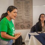 Mulher fala durante uma reunião ou oficina realizada em ambiente interno.