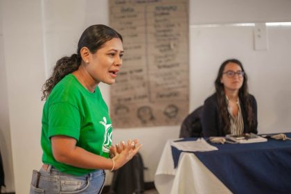 Mulher fala durante uma reunião ou oficina realizada em ambiente interno.