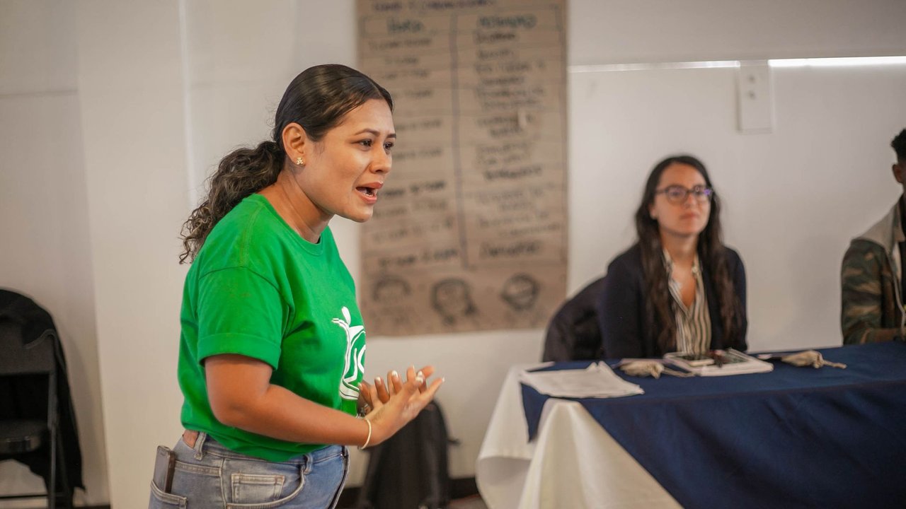 Mulher fala durante uma reunião ou oficina realizada em ambiente interno.