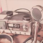 Microfone vintage, aparelho de rádio e fones de ouvido sobre uma mesa de madeira.