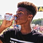 Homem jovem bebe água engarrafada ao ar livre durante um evento esportivo.