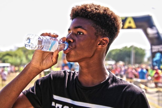 Homem jovem bebe água engarrafada ao ar livre durante um evento esportivo.