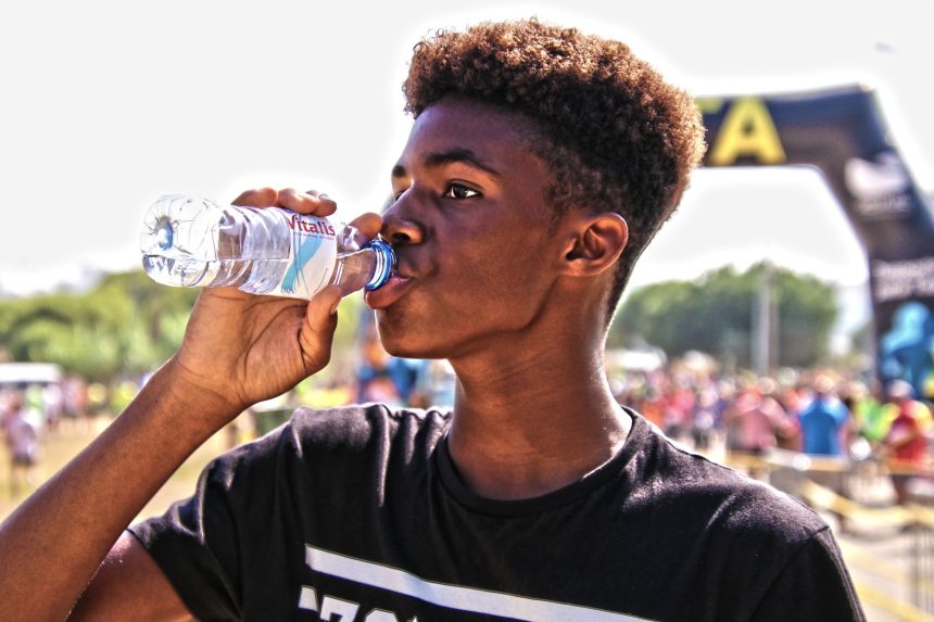 Homem jovem bebe água engarrafada ao ar livre durante um evento esportivo.